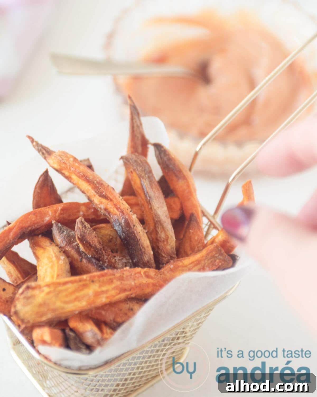 Crispy Air Fryer Sweet Potatoes with Creamy Dipping Sauce 2 A hand taking a sweet potato fries from a golden chip tray with baking paper (which is filled with fries) in the background a dipping sauce