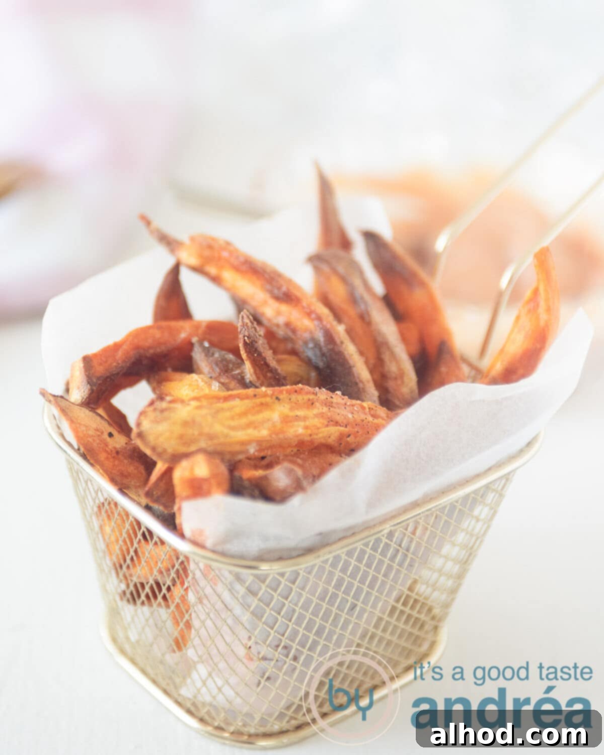 Crispy Air Fryer Sweet Potatoes with Creamy Dipping Sauce 8 In the middle a golden fries tray in which a baking paper is folded with sweet potato fries in it