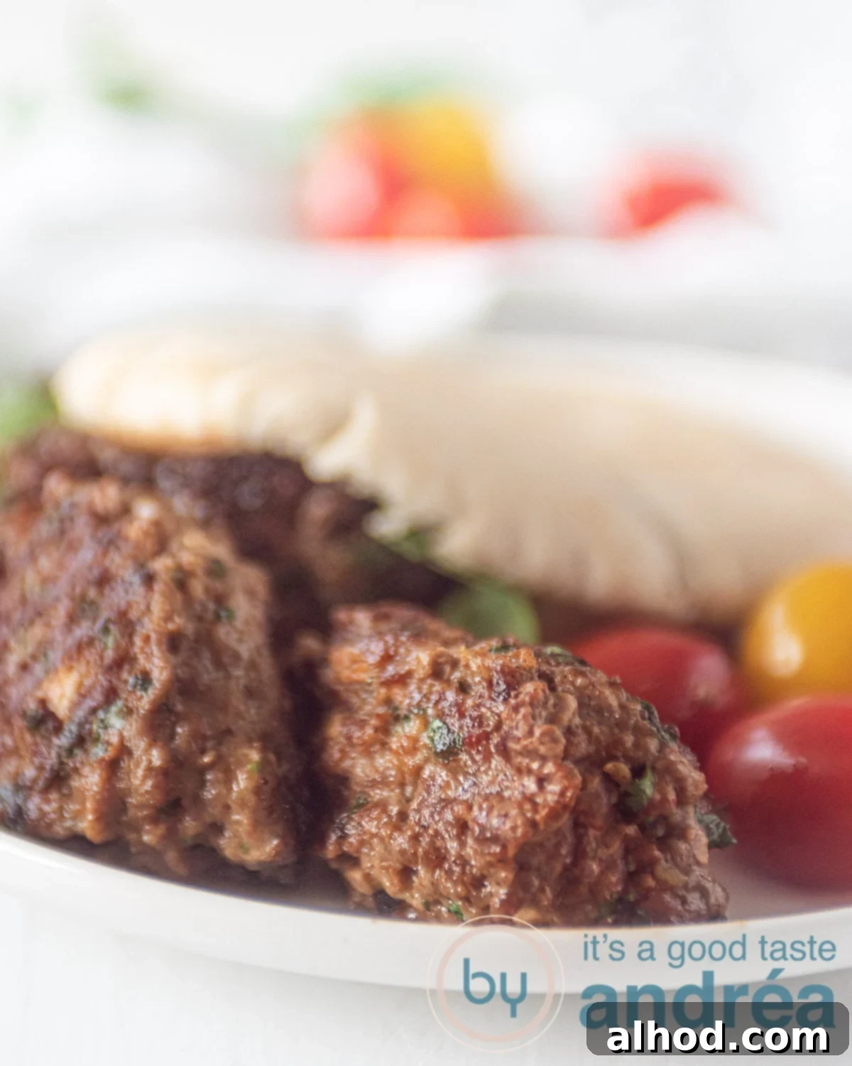 Cevapi: Serbia's Iconic Grilled Sausage 2 detail shot of cevapi in a pita bread on a white plate. Some tomatoes around it.