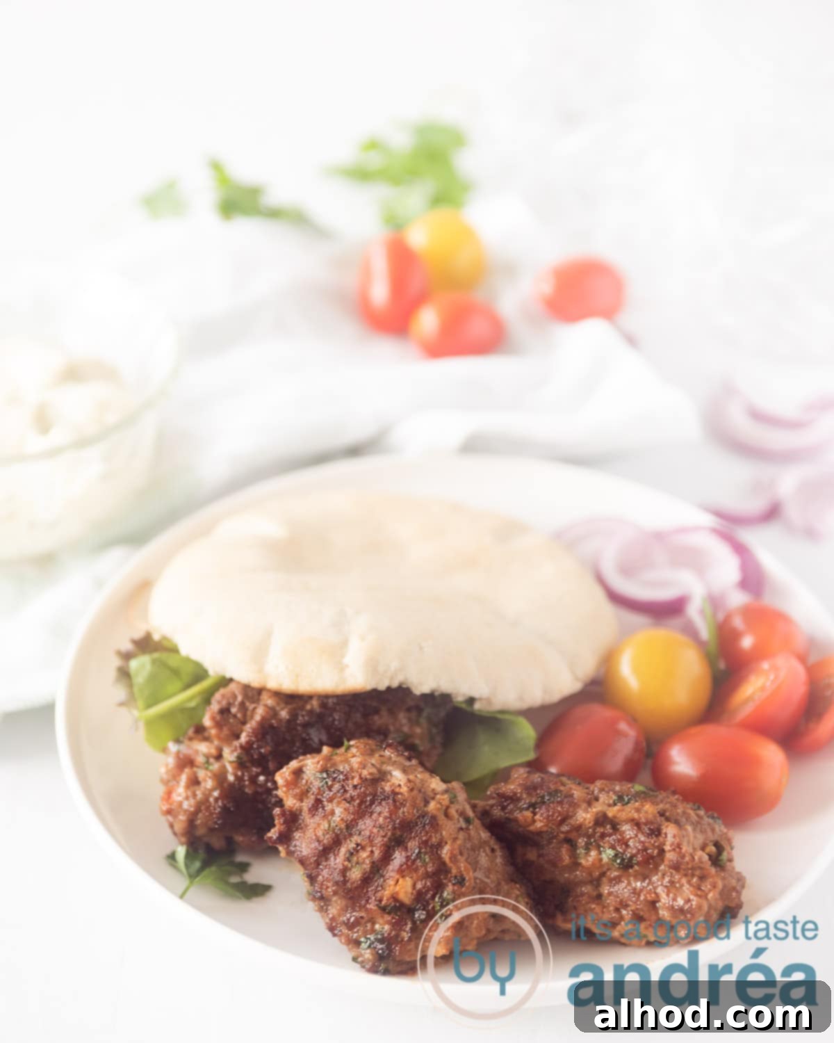 Cevapi: Serbia's Iconic Grilled Sausage 5 A white plate with a pita bread filled with cevapi, lettuce and tomatoes. What vegetables are around the plate