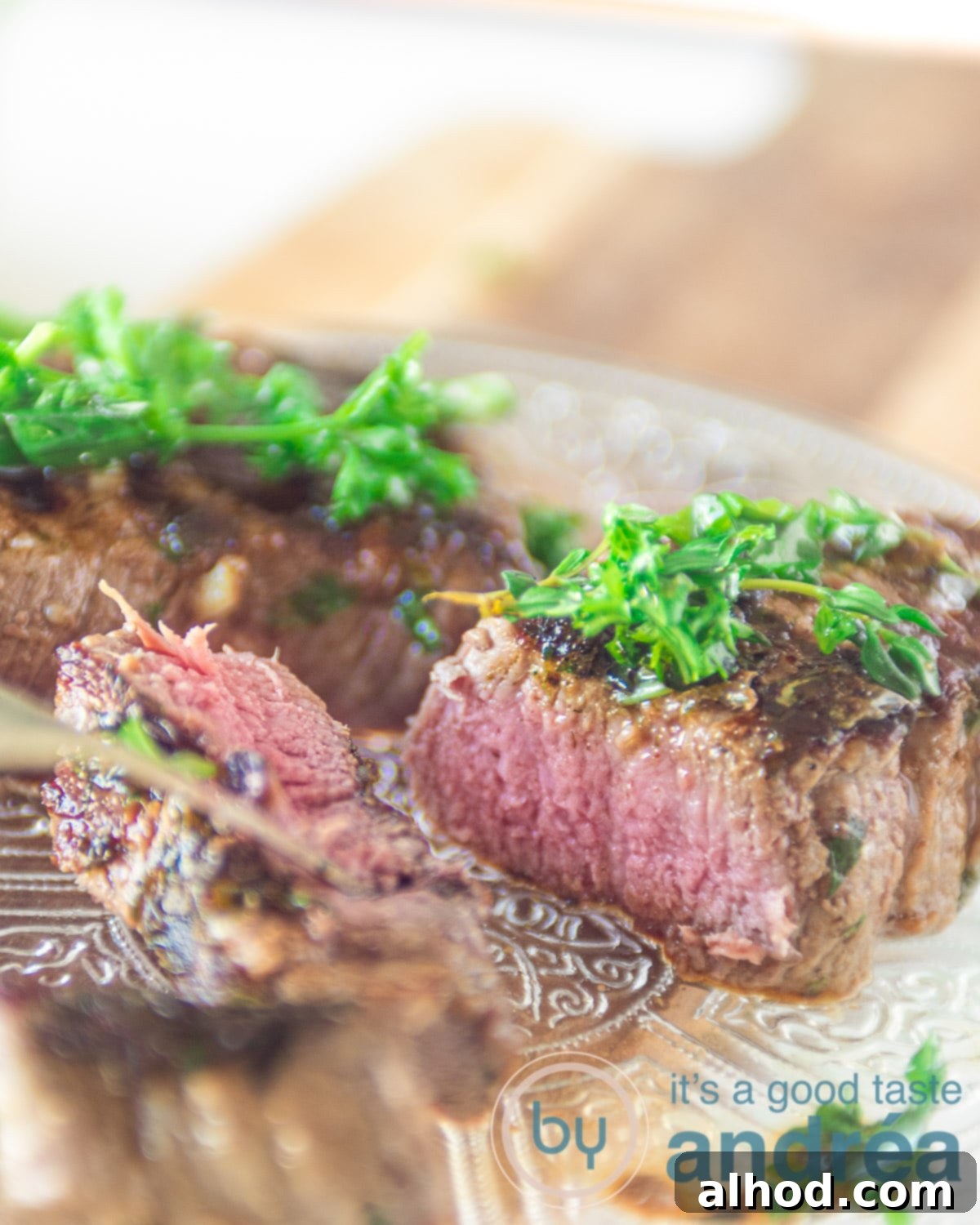 Green Herb Marinated Grilled Flat Iron Steak 5 A beautifully sliced flat iron steak arranged on a glass plate, garnished with fresh herbs, ready to be served on a wooden board.