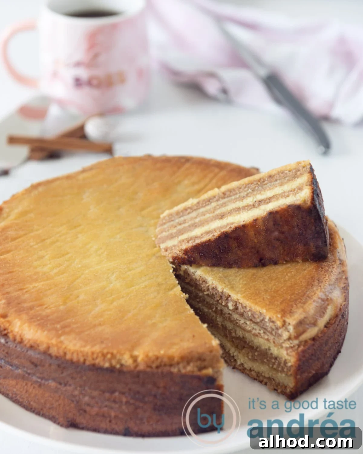 A beautifully round Indonesian Thousand Layers Cake (Lapis Legit) with a slice cut out, showcasing its numerous delicate layers. The slice is placed on top of the cake, with a cup of coffee and a knife in the background, ready to be enjoyed.