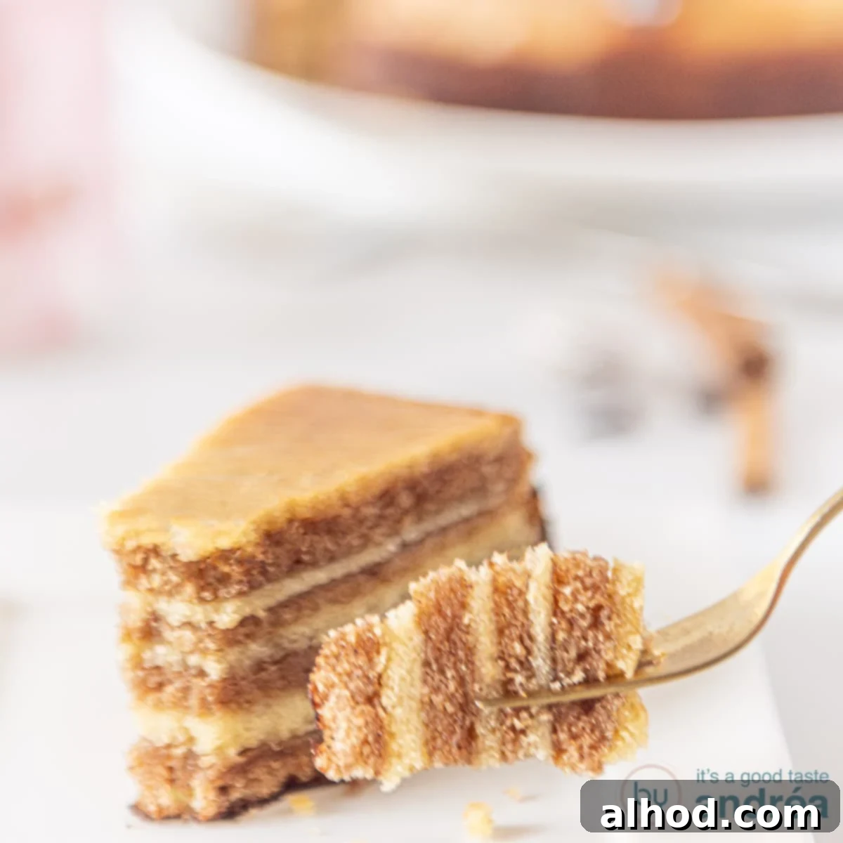 A square picture with a piece of thousand layers cake on a white plate. A fork holding a piece.