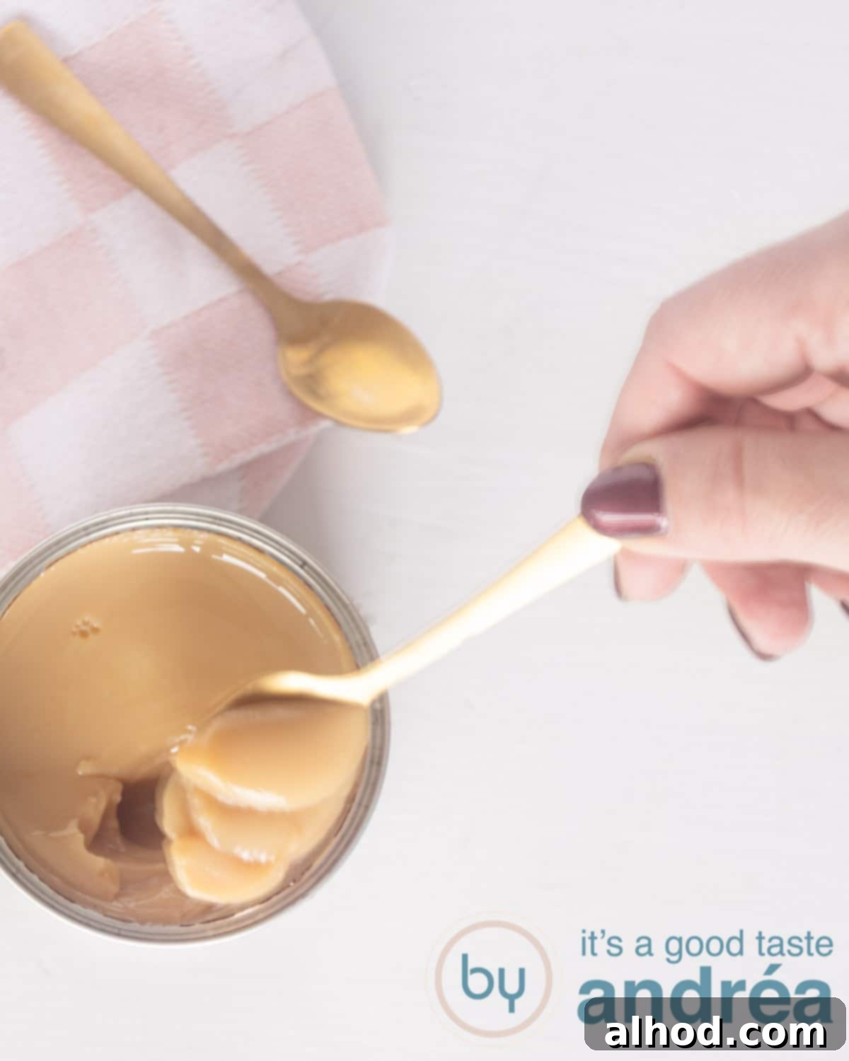 Dulce de Leche from Condensed Milk Six Easy Ways 2 A top photo of homemade dulce de leche with a spoon taken a bit out of the tin. A pink cloth and golden spoon in the top.