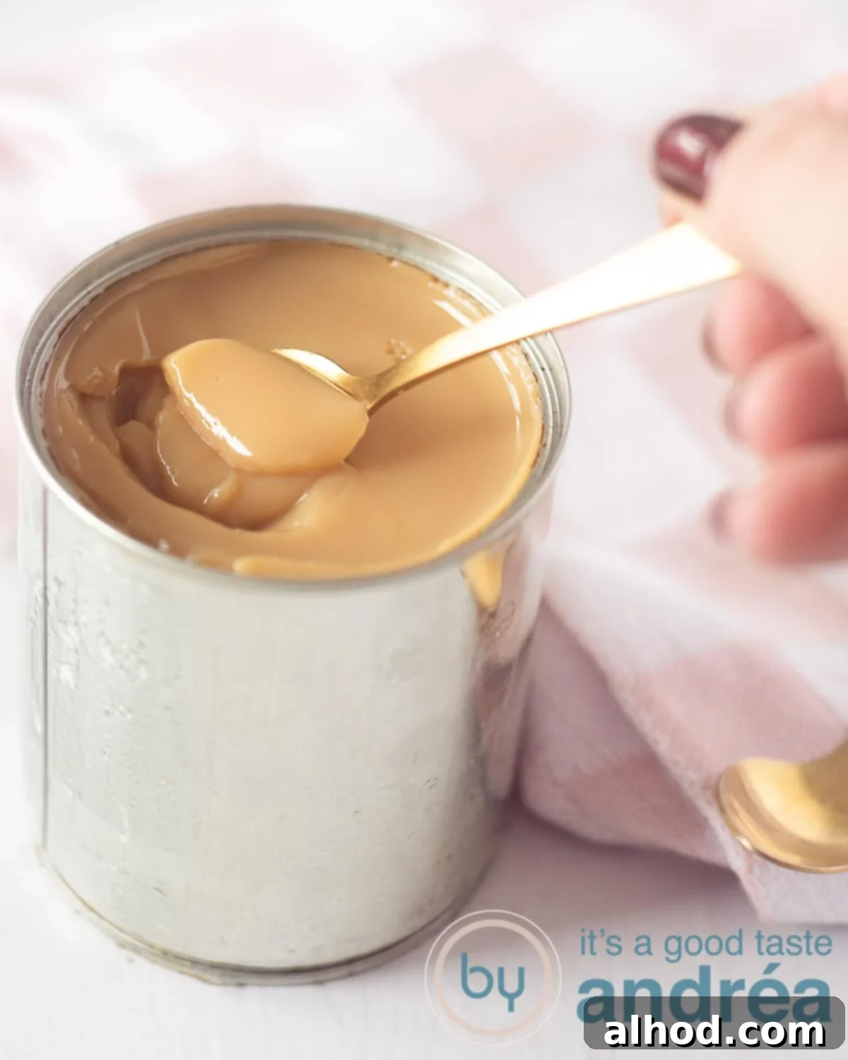 Dulce de Leche from Condensed Milk Six Easy Ways 5 A tin filled with creamy dulce de leche. A golden spoon takes a bit out of the tin. A pink cloth in the background