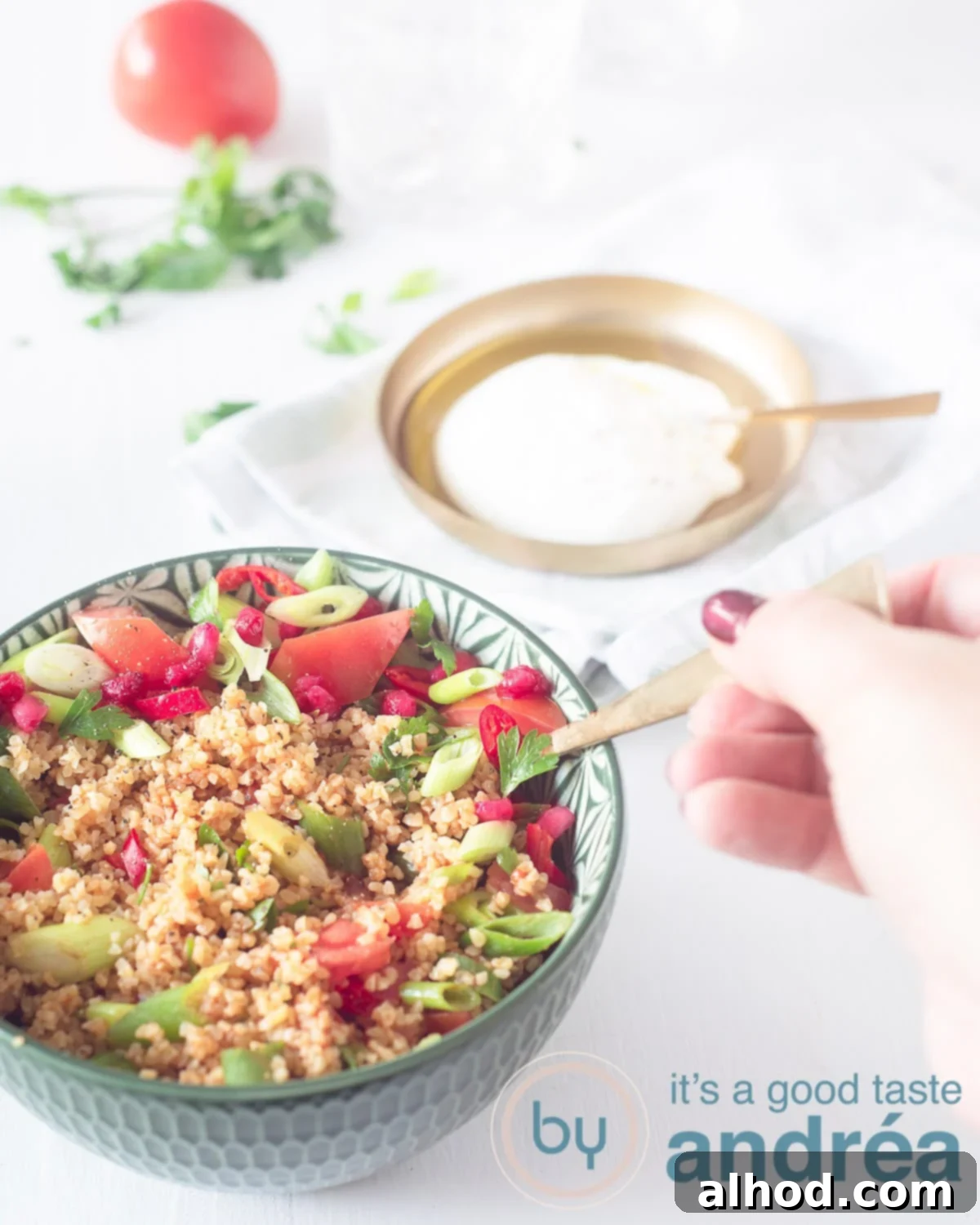 The Essential Turkish Kisir A Flavorful Bulgur Salad 5 A delicious Kisir salad from above in a green bowl, with a hand reaching in to take a bite. In the background, a crème fraîche dip and some garnish.