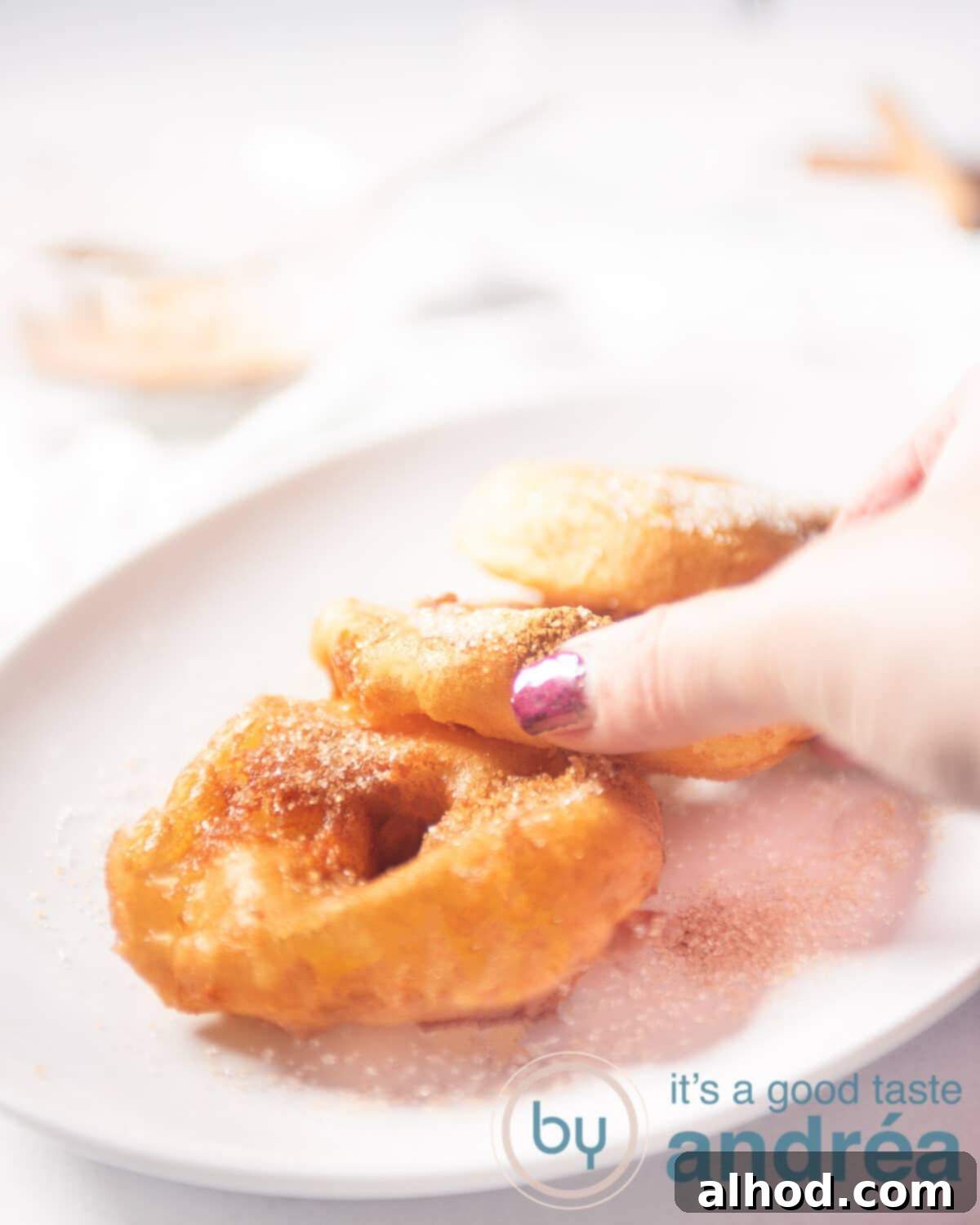 Traditional Dutch Apple Doughnuts 5 A hand taking an apple fritter from a white bowl with three fritters