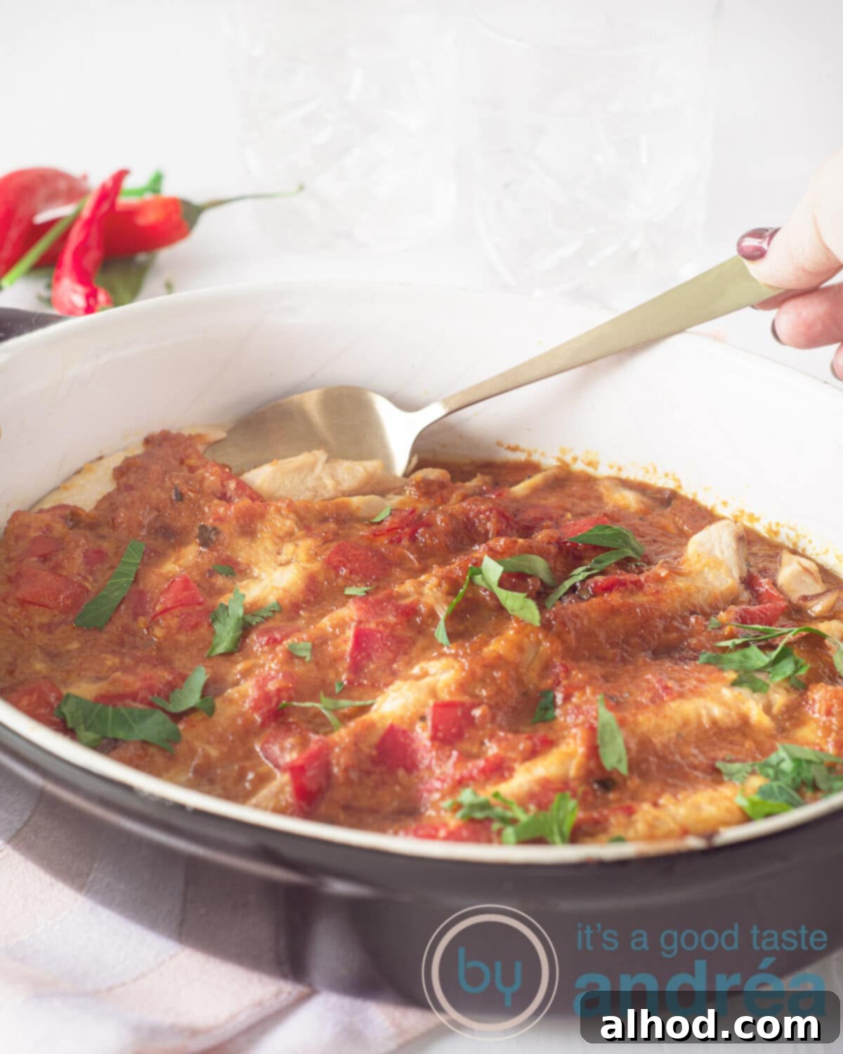 Pepesan Ikan Fiery Indonesian Mackerel 5 A hand holding a spoon delicately lifting a piece of spicy mackerel from a black oven dish, ready to be served. Peppers are blurred in the background.