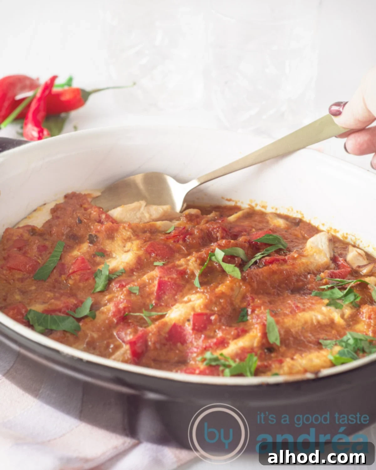Pepesan Ikan Fiery Indonesian Mackerel 6 A hand holding a spoon that wants to grab a mackerel from the baking dish. The oven dish is black on the outside. Some peppers in the background