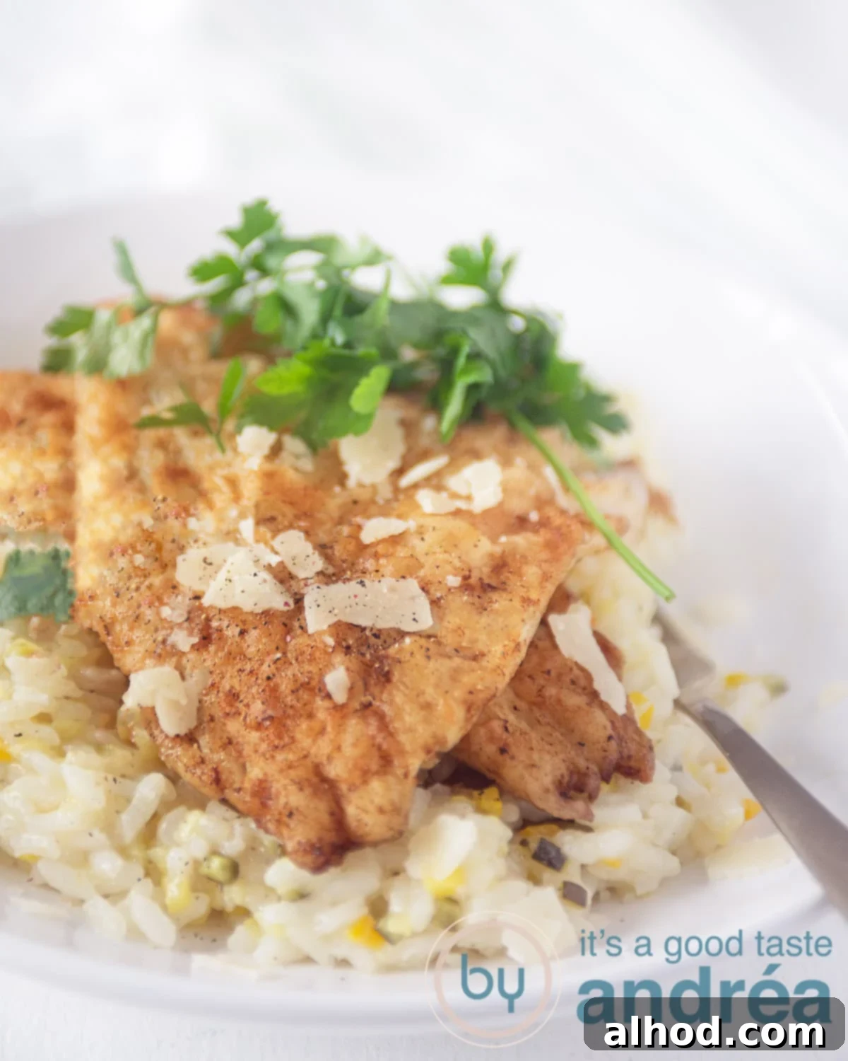 Flaky Cod and Fresh Zucchini Risotto 6 Photo of a white plate with a gold spoon. The plate is filled with risotto with zucchini and cheese. On top of that are two slices of fried cod