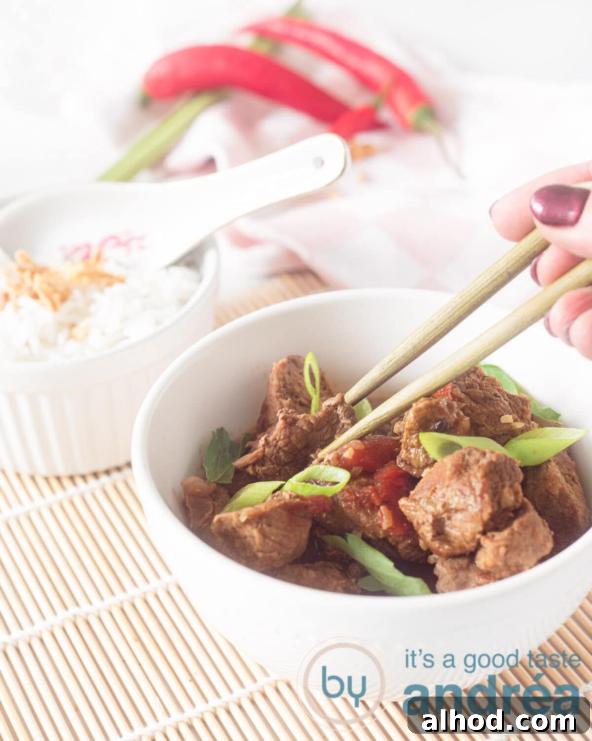 Sweet & Savory Slow-Simmered Beef 5 A white bowl filled with Indonesian beef stew (Semur Daging) braised in Kecap, with a separate bowl of fluffy white rice in the background, all arranged on a woven wicker mat.