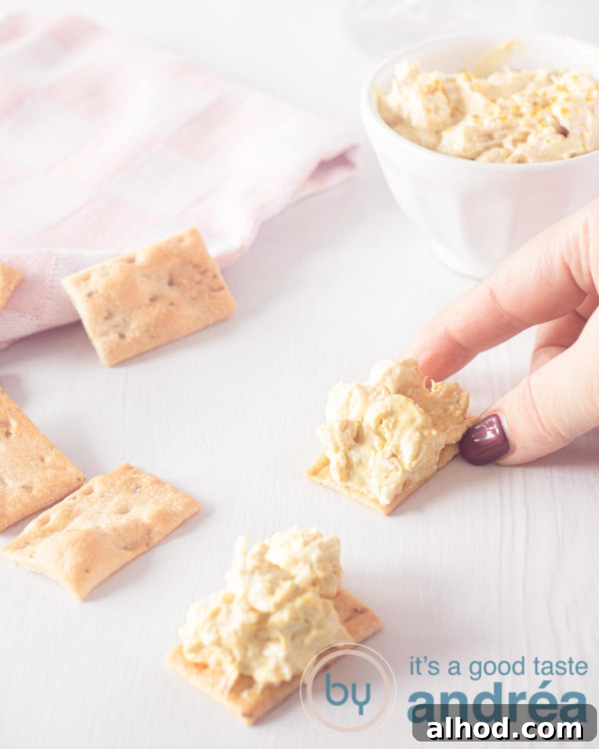 The Ultimate Curry Chicken Salad Sandwich 5 A hand grabbing a toast with chicken curry salad. A second piece of toast lies underneath. In the top left corner a pink white striped cloth and in the top right the rest of the salad