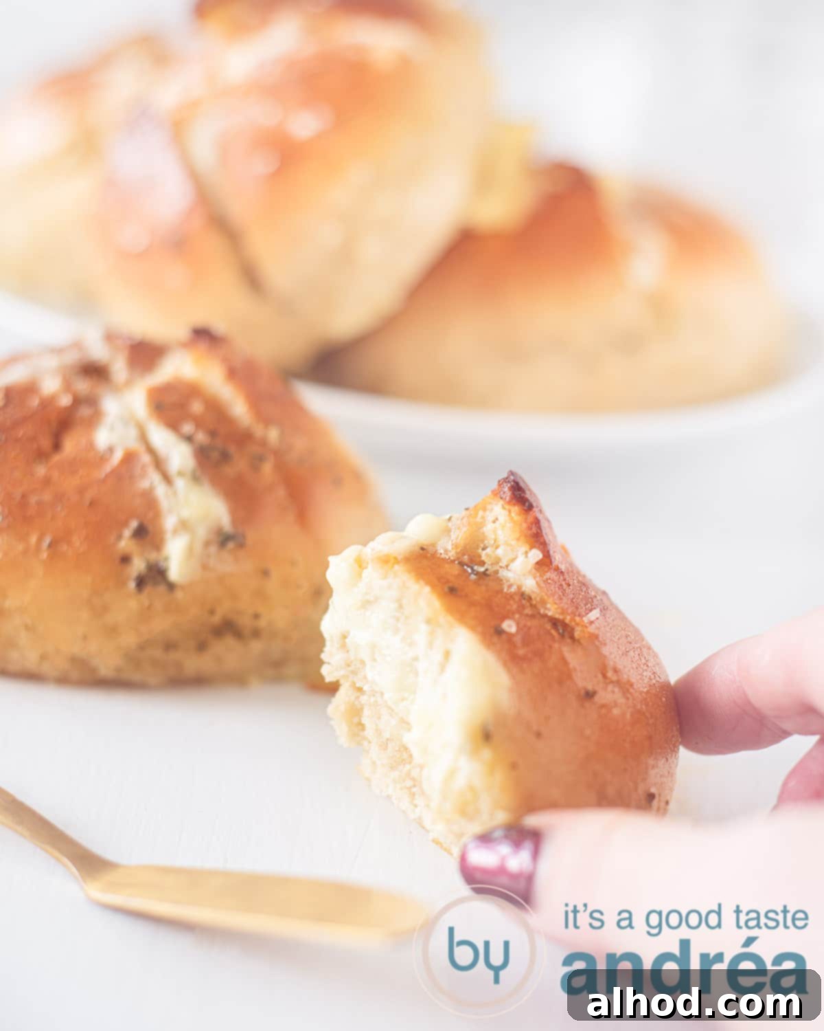 Mouthwatering Korean Cream Cheese Garlic Bread 2 A hand taking a wedge of Korean Garlic Cream cheese bread. Three breads are in the background. A white backdrop