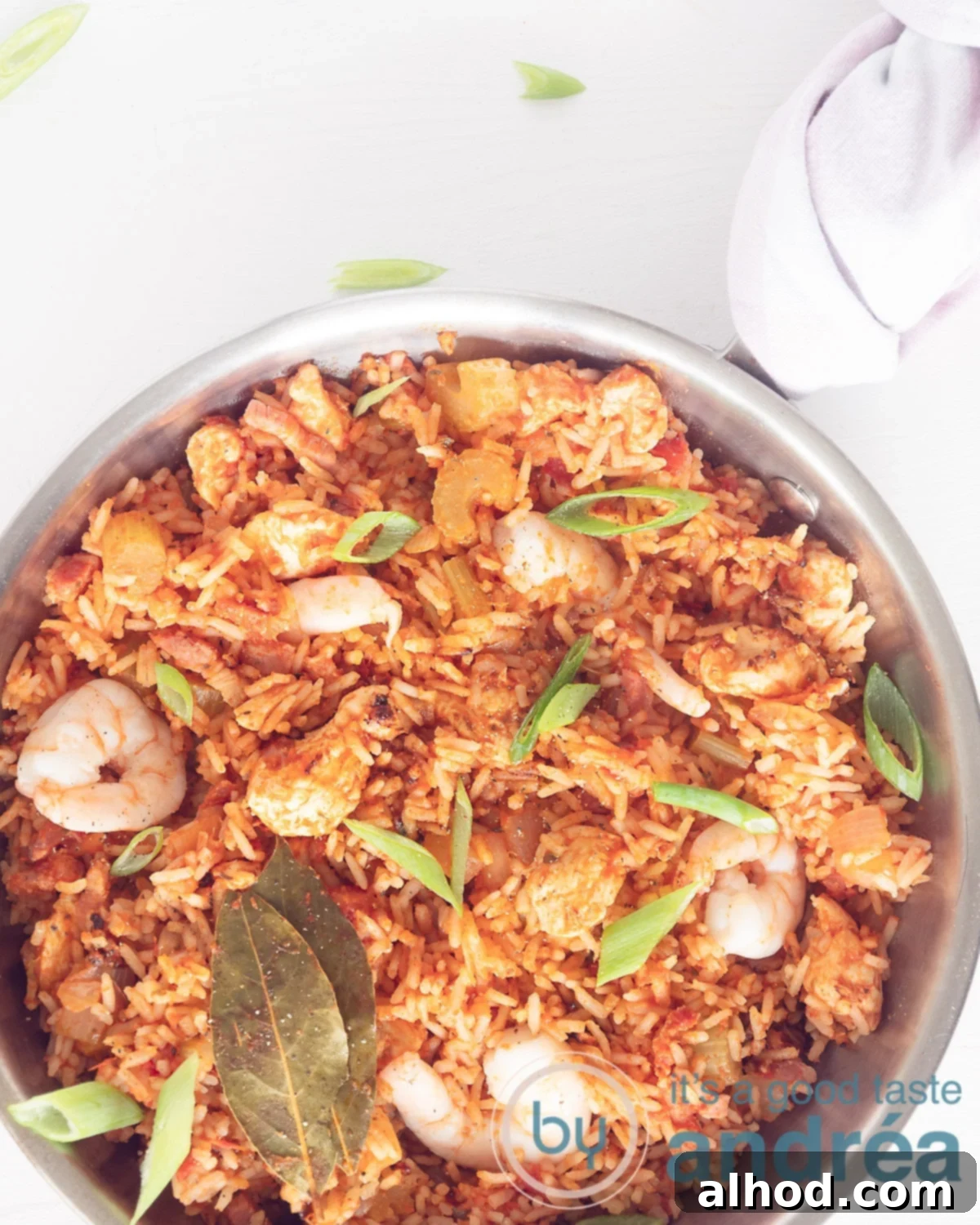Classic Chicken, Shrimp and Sausage Jambalaya 2 A photo from above of an aluminum pan filled with rice, shrimp, tomatoes, chicken and garnished with spring onions. On a white background