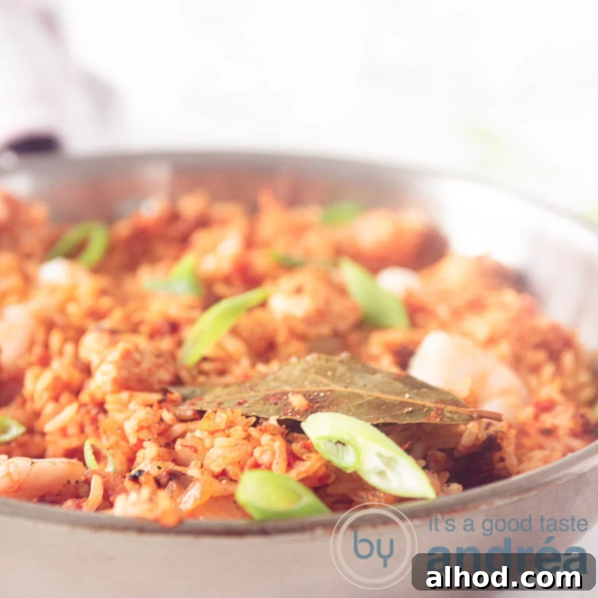 Classic Chicken, Shrimp, and Sausage Jambalaya Recipe 6 A frying pan with jambalaya, shrimp and spring onions on a white surface. A square photo
