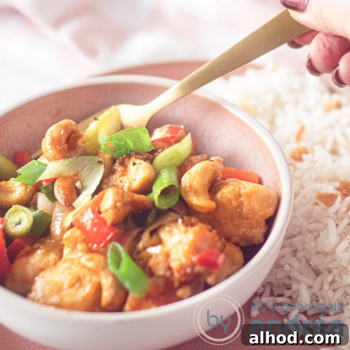 15 Minute Spicy Cashew Chicken 6 A pink bowl with chicken Siam and a gold spoon. Next to it is rice, and in the background is a pink and white tea towel.