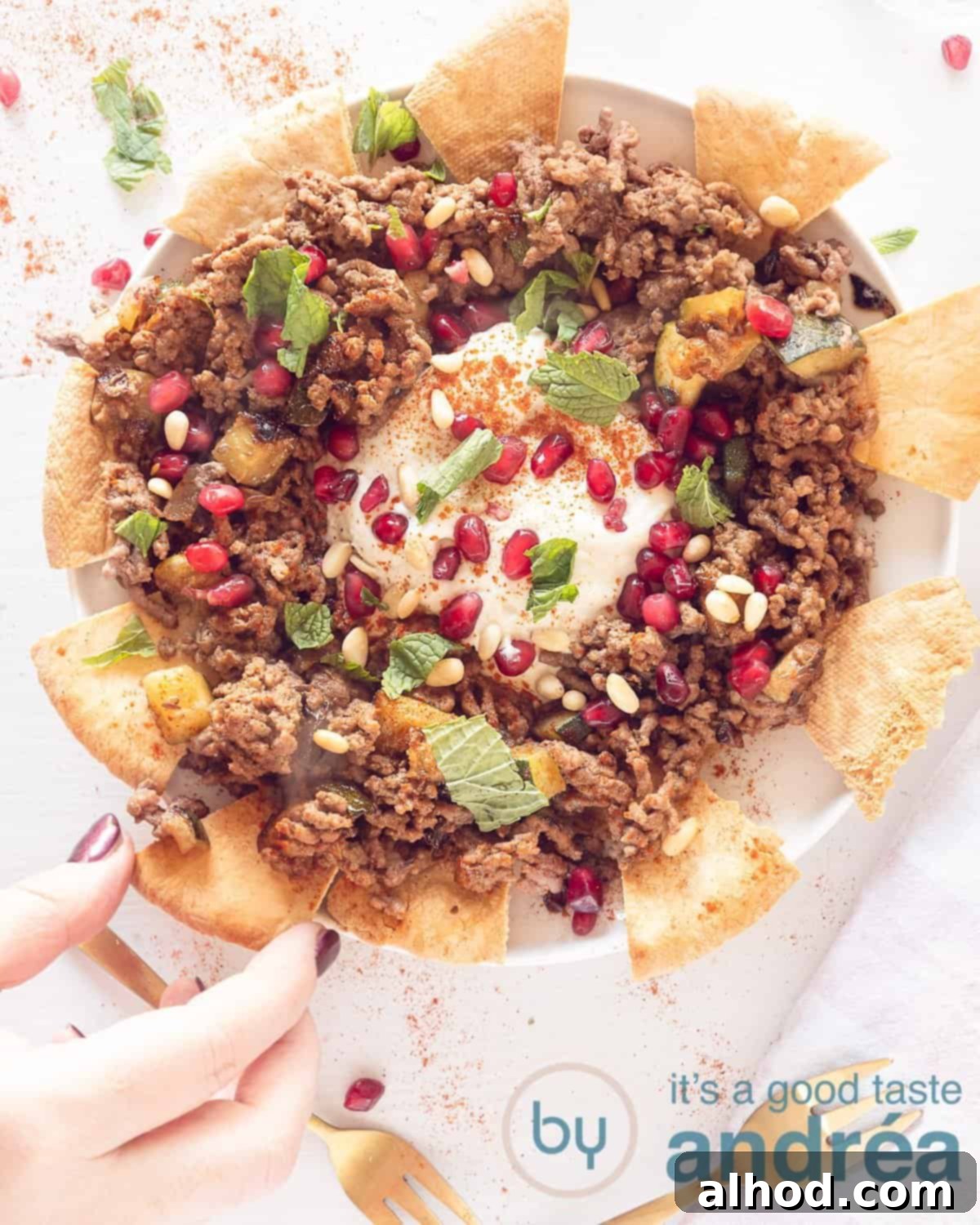 Kabaklı Kıymalı Fatteh Ortadoğu Sofralarının Gözdesi 5 A photo from above of a plate filled with pita and Lebanese spiced ground beef with yogurt dip. A hand takes a point.