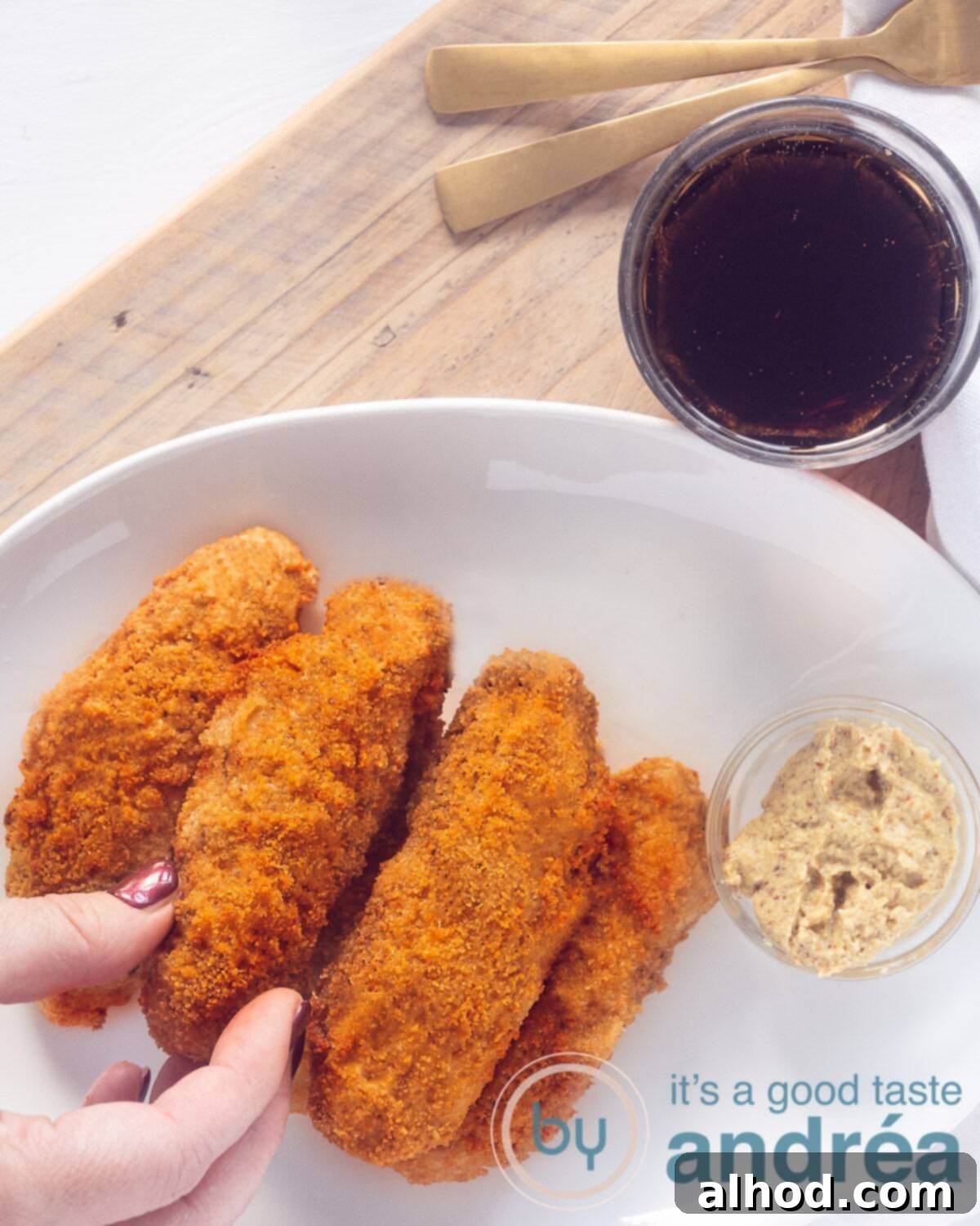 A hand taking a kroket from a white bowl (with five croquettes) on a wooden board. A glass of Coke is above it