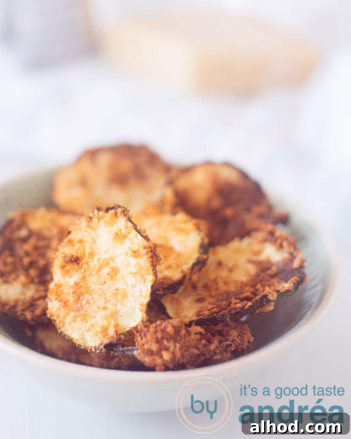 Crispy Air Fryer Zucchini Chips with Parmesan 2 A bowl full of crispy zucchini chips gratin with parmesan cheese, ready to be enjoyed. In the background, fresh Parmesan cheese and a grater hint at the delicious ingredients.