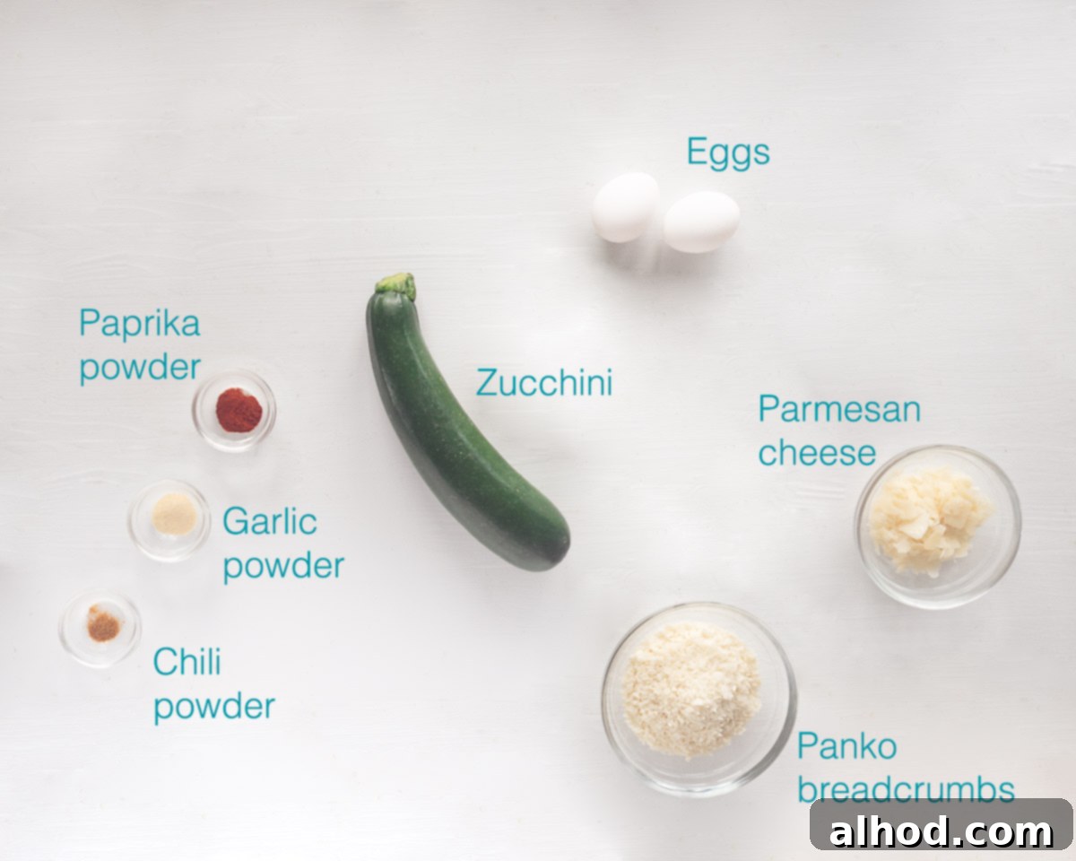 Crispy Air Fryer Zucchini Chips with Parmesan 3 A flat lay of fresh ingredients for Air Fryer Zucchini Chips including zucchini, a bowl of Panko, a bowl of grated Parmesan, an egg, and small dishes of spices like garlic powder, paprika, and chili powder.