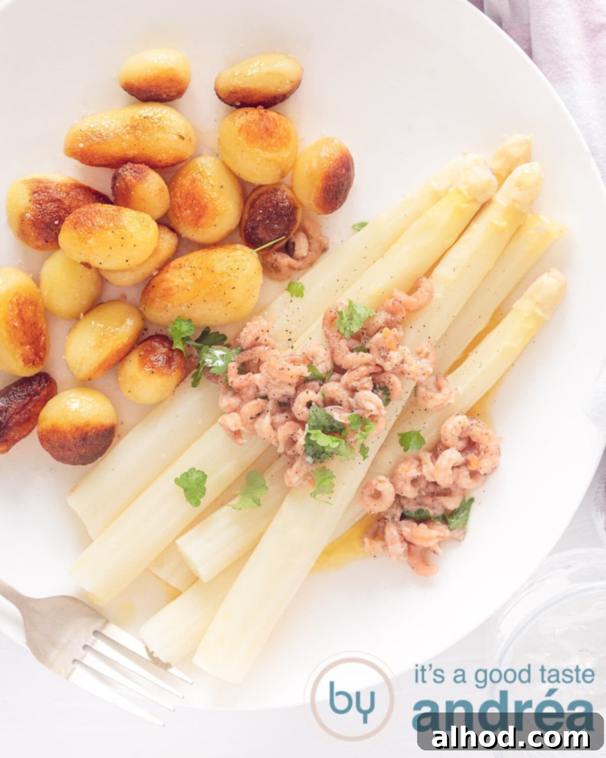 Tender German White Asparagus with Melted Butter 2 A top-down view of a white plate generously topped with golden-fried baby potatoes, tender white asparagus spears, and succulent cocktail shrimp, all glistening under a rich butter sauce and garnished with fresh parsley.