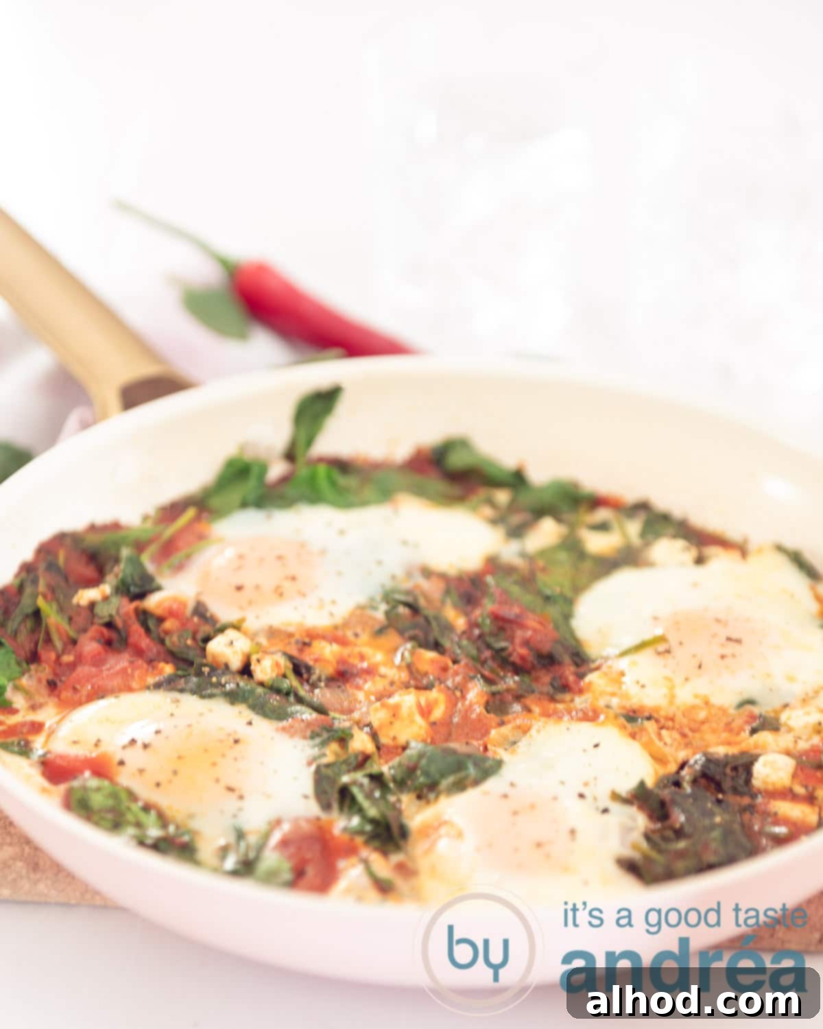 Simple Spinach and Feta Shakshuka 3 A pink pan filled with poached eggs in a tomato sauce, spinach and feta on a white background