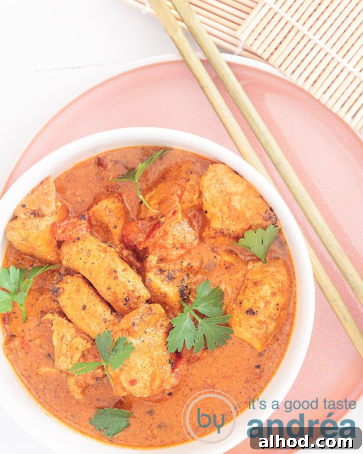 Effortless Slow Cooker Butter Chicken 2 A photo from above of chicken with buttery curry sauce on a pink plate. Two chopsticks are right next to it, inviting you to taste this creamy slow cooker butter chicken.