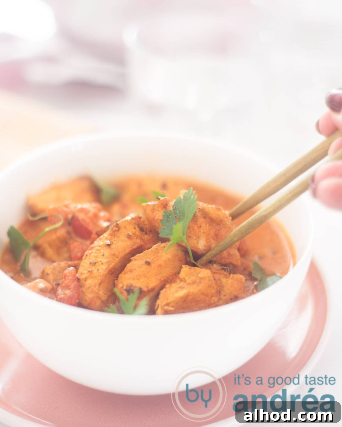 Effortless Slow Cooker Butter Chicken 5 An elevation photo with a white bowl containing Indian Murgh Makhani. Two chopsticks gracefully grab a cube of chicken, ready to enjoy. A clean white background highlights the dish.