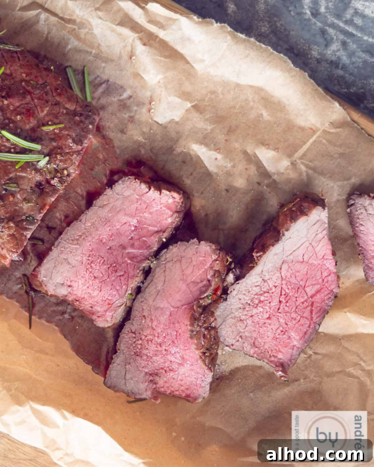 Slow-Roasted Herb-Crusted BBQ Beef 3 A photo from above of a succulent roast beef, artfully arranged on baking paper with fresh herbs, showcasing its rich texture and color.