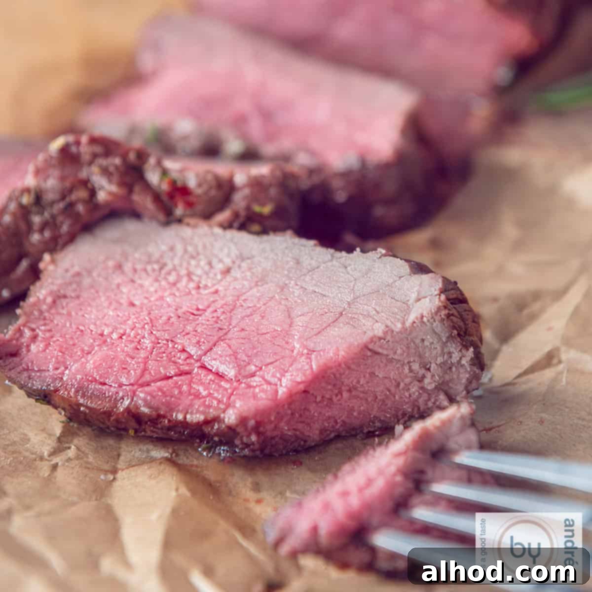 Slow-Roasted Herb-Crusted BBQ Beef 4 A square photo with slices of roast beef on baking paper with a piece cut off