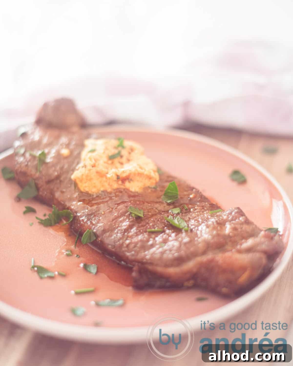 Effortless Air Fryer Sirloin Steak 2 A pink plate on a wooden shelf with a pink and white checkered tea towel behind it. On the plate sirloin steak with herb butter and parsley