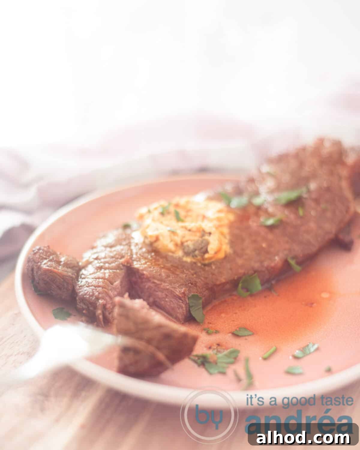 Effortless Air Fryer Sirloin Steak 6 Een hoogtefoto met een roze bord op een houten plank. Een lapje entrecote met een stukje er van af gesneden met een vork. Kruidenboter smelt erbovenop