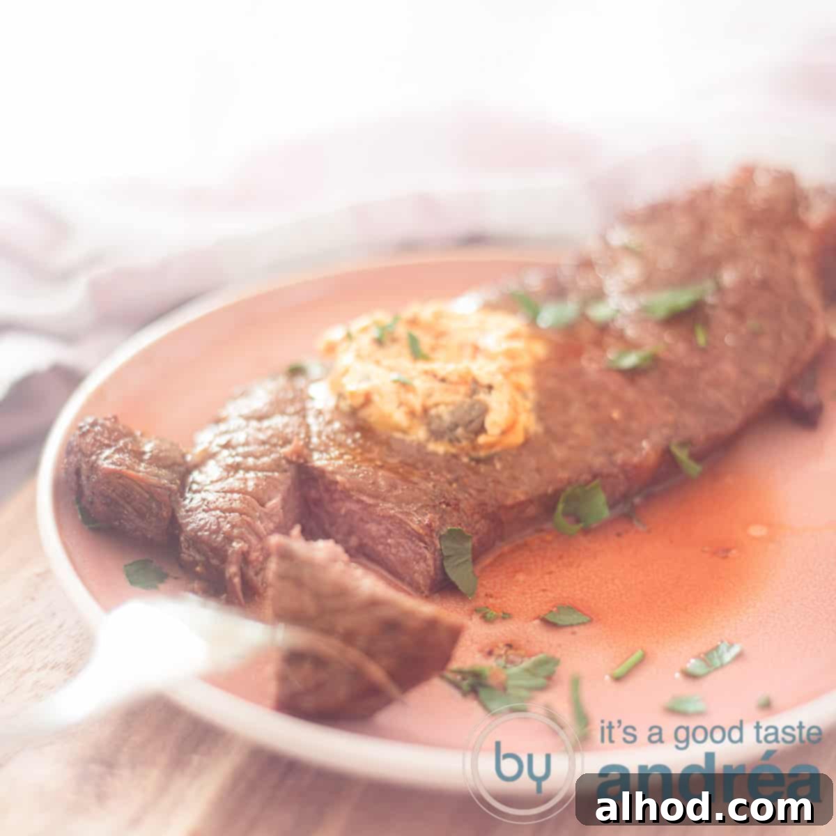 Effortless Air Fryer Sirloin Steak 7 A square photo with a piece of sirloin steak with a piece cut off on a pink plate. Herb butter melts on the sirloin steak