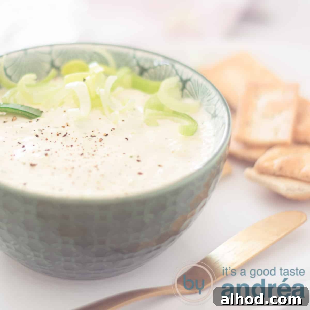 Dutch Farmhouse Leek Dip 6 A square photo with a cream cheese herb dip in a green dish. In front of it a golden knife. Some toast in the back