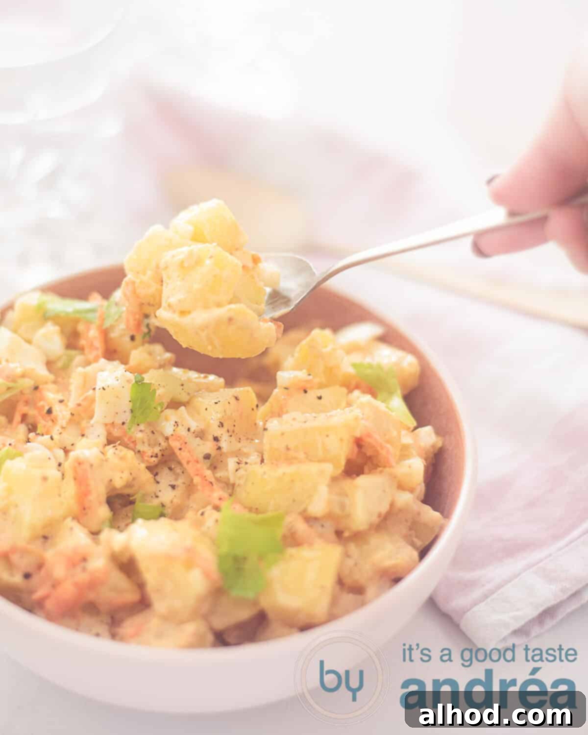 Amish Potato Salad 5 An appetizing close-up of creamy Amish potato salad with chunks of egg, perfectly portioned with a spoon, set against a background of a pink and white tea towel.