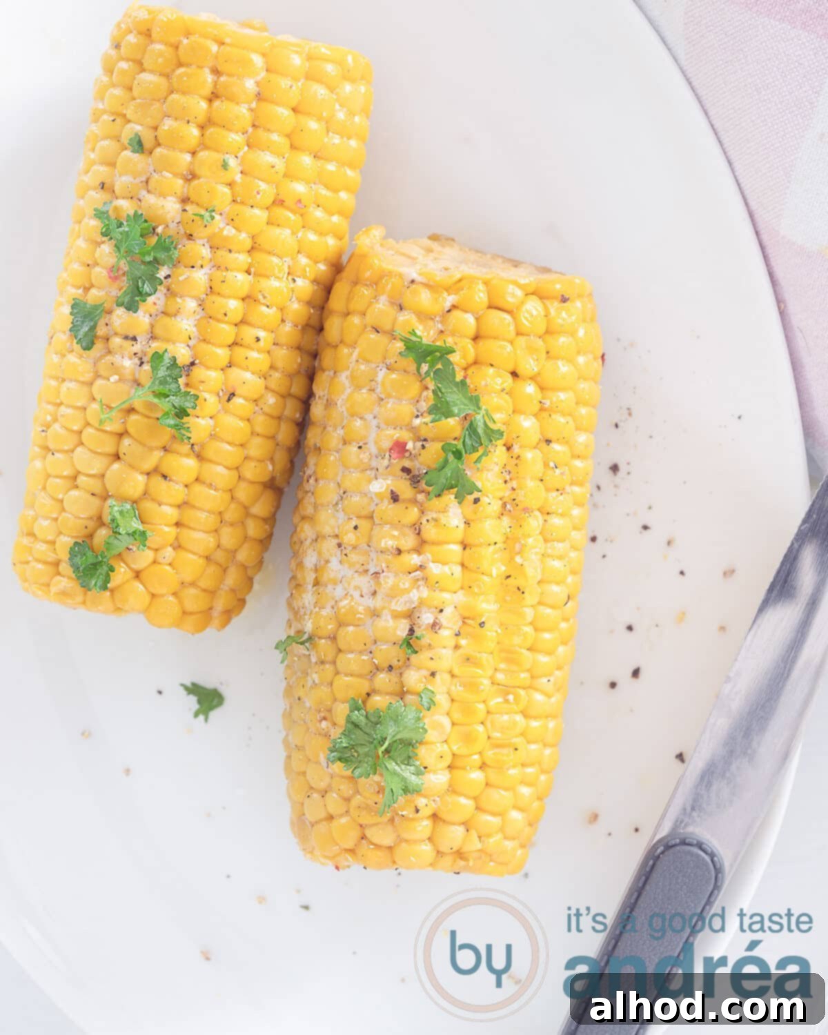 Fire-Kissed Bourbon Butter Corn 2 Two perfectly cooked bourbon butter grilled corn cobs, garnished with fresh parsley, salt, and pepper, next to a chef's knife.
