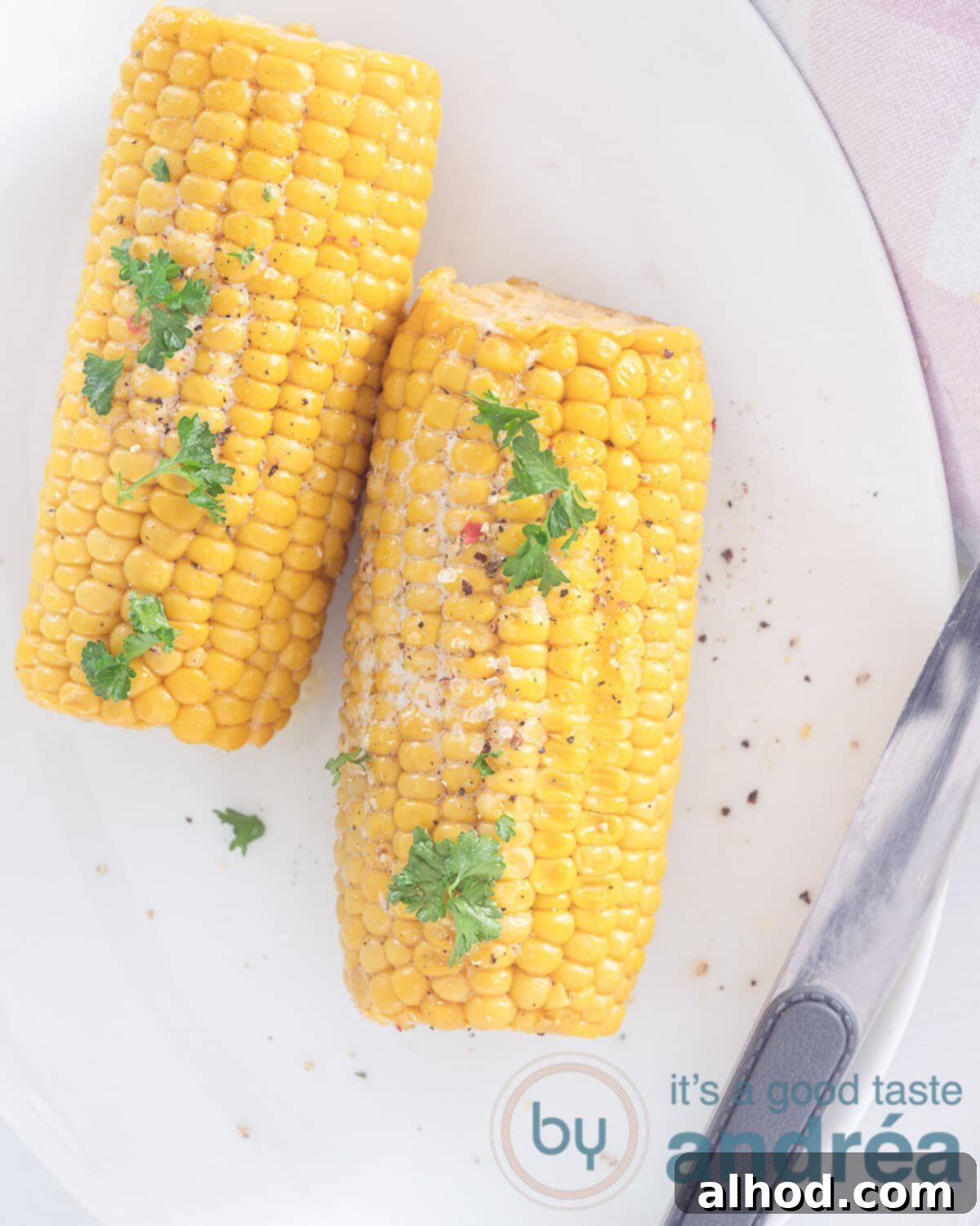 Bourbon Butter Glazed Grilled Corn 2 A photo from above of two corn on the cob with parsley, salt and pepper. a knife at the bottom