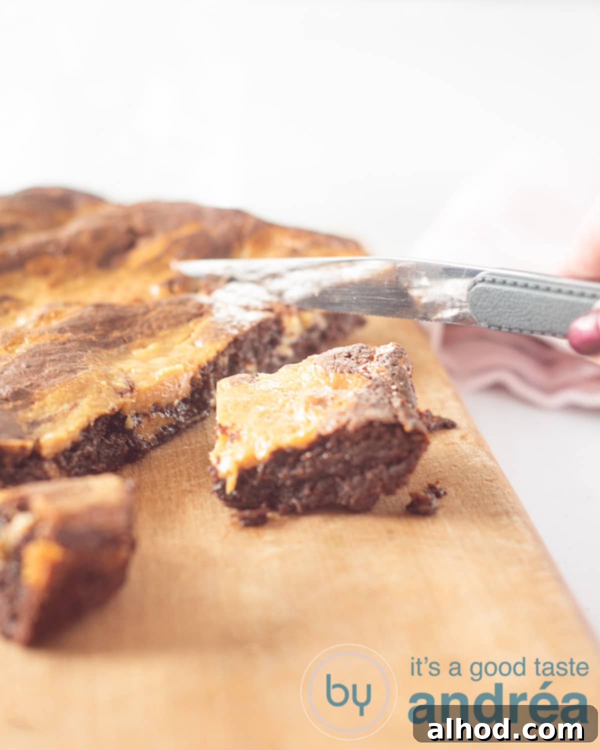 Decadent Caramel Brownies 2 A hand slicing a rich, fudgy caramel brownie with dulce de leche swirl into perfect cubes on a rustic wooden board.
