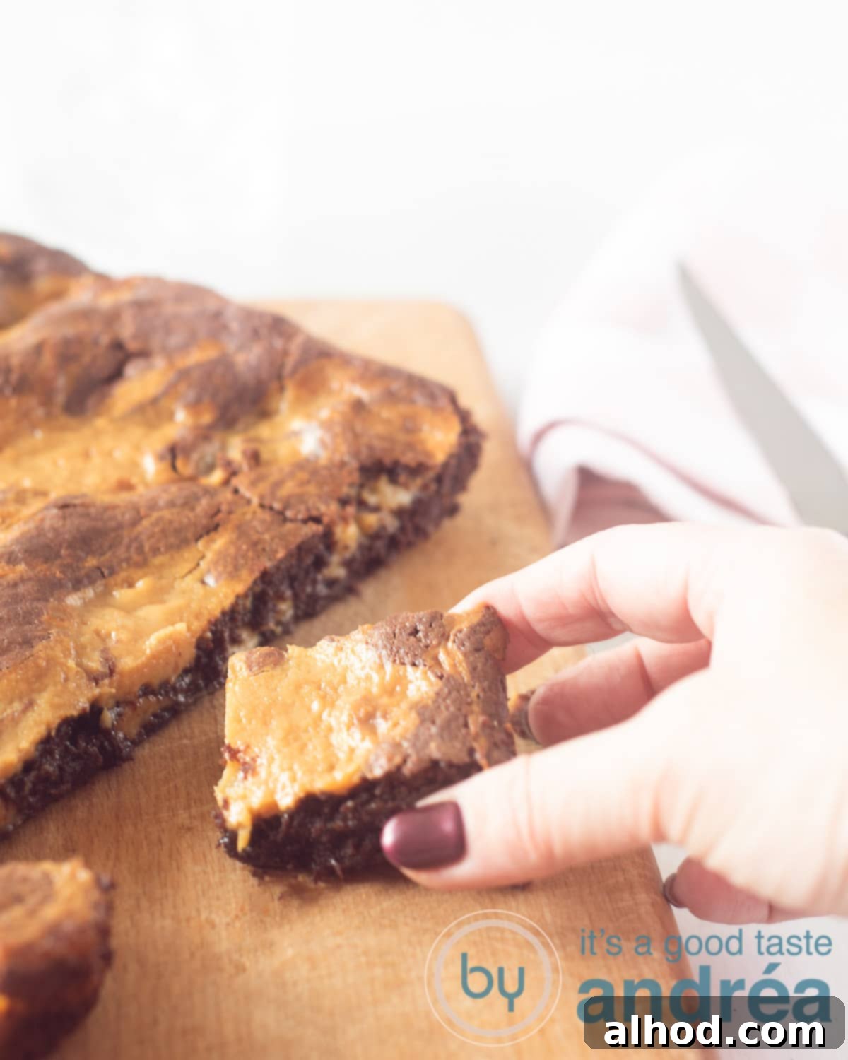 Decadent Caramel Brownies 5 A rich, fudgy caramel brownie with dulce de leche swirl on a wooden board, with a hand reaching for a cut piece.