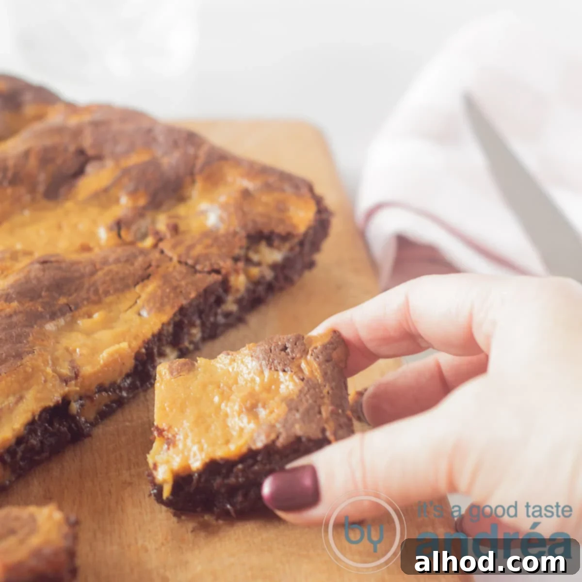 Decadent Caramel Brownies 6 A square photo with a fudgy caramel brownie with a piece cut off. A cube of dulce de leche brownie is removed from the cutting board.