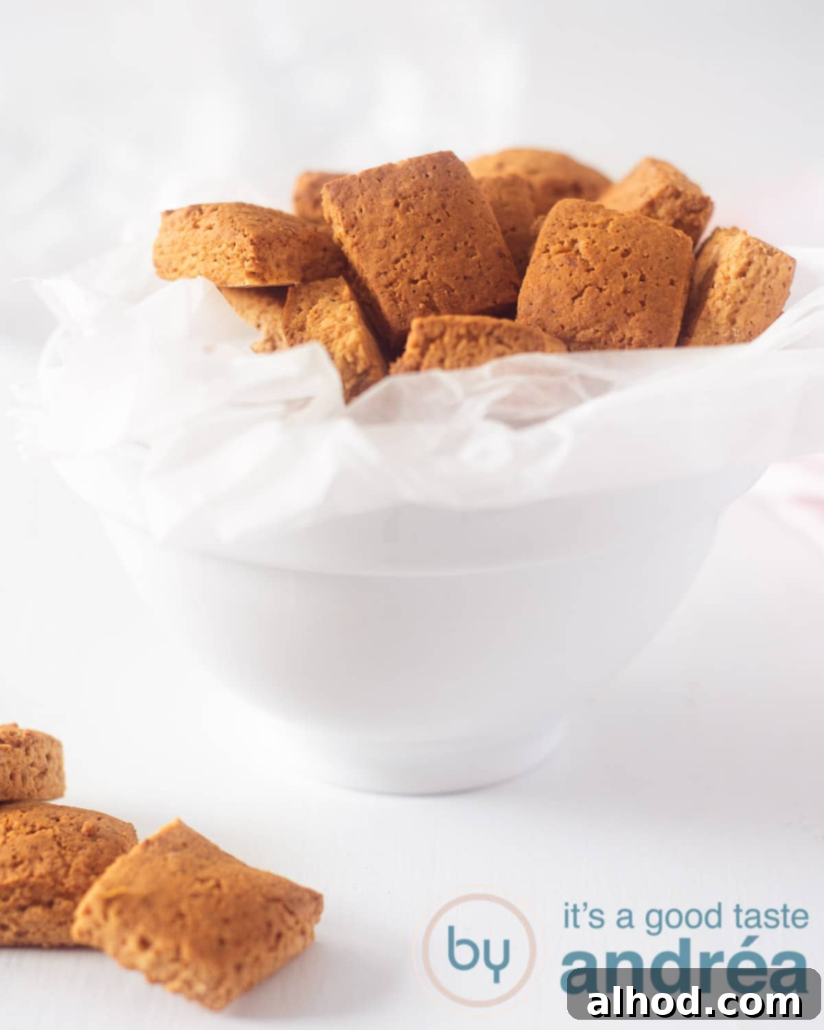 Dutch Pepernoten: Spiced Cookie Delights 2 A white tray with baking paper in which gingerbread cookies lie on a white background. In the foreground three gingerbread cookies