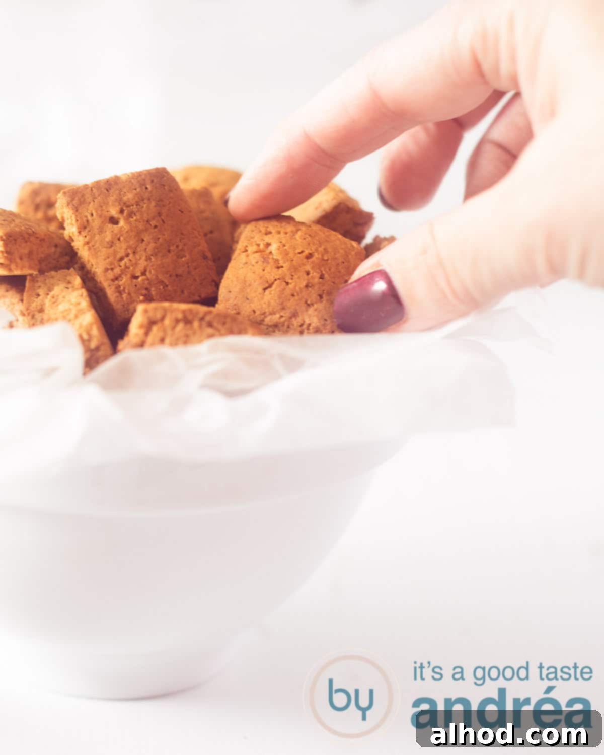 Dutch Pepernoten: Spiced Cookie Delights 5 A white bowl with Old Dutch gingerbread cookies. A hand that takes a gingerbread