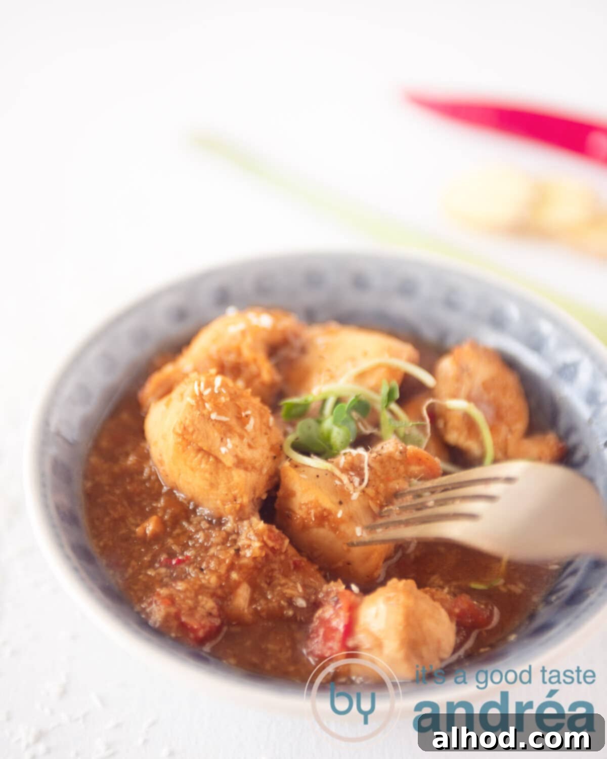 Balinese Spiced Chicken Ayam Bumbu Bali 2 A gray plate with chicken pieces and a golden fork taking out a piece. A white background and in the background a piece of pepper, ginger and lemongrass