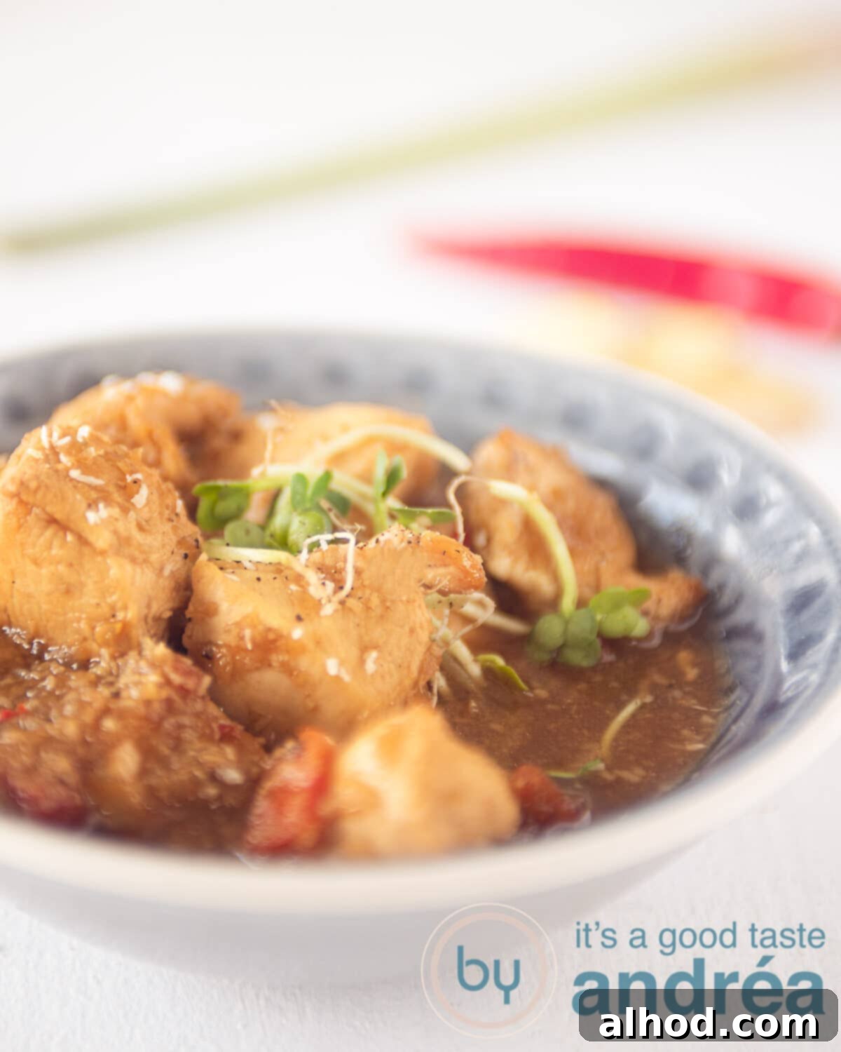 Balinese Spiced Chicken Ayam Bumbu Bali 5 A gray plate filled with chicken in a spicy sauce on a white background. In the background a pepper, ginger and lemongrass