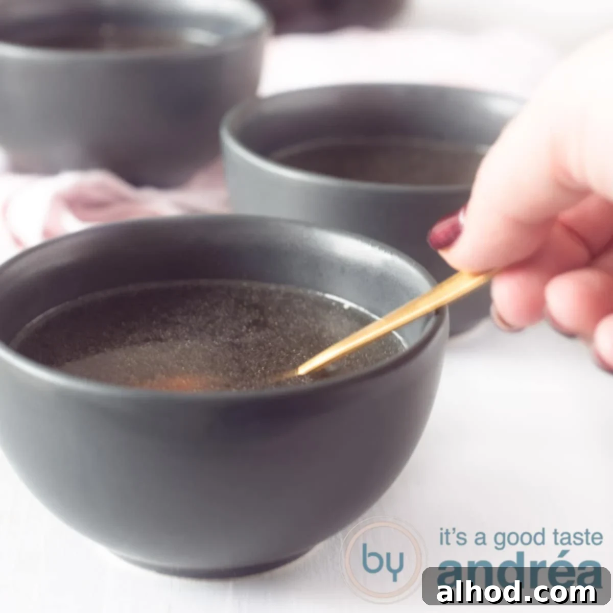 Nourishing Slow Cooker Chicken Bone Broth 6 A square photo with gray bowls of chicken stock. A hand with a golden spoon takes a bite.