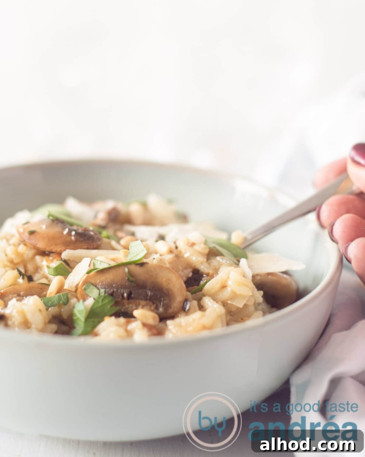 Earthy Mushroom Risotto 5 A bowl filled with risotto with mushrooms, a golden spoon grabs a bite. A white background