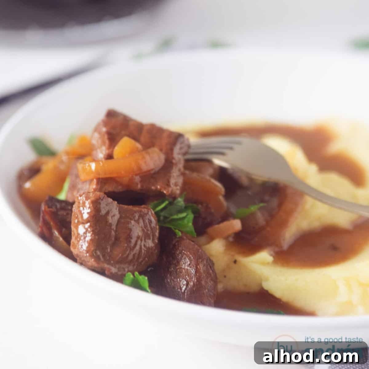 Classic Dutch Hachee Beef and Onion Stew 6 A square photo showing part of a deep white plate of mashed potatoes and hachee (Dutch beef stew). On a white background