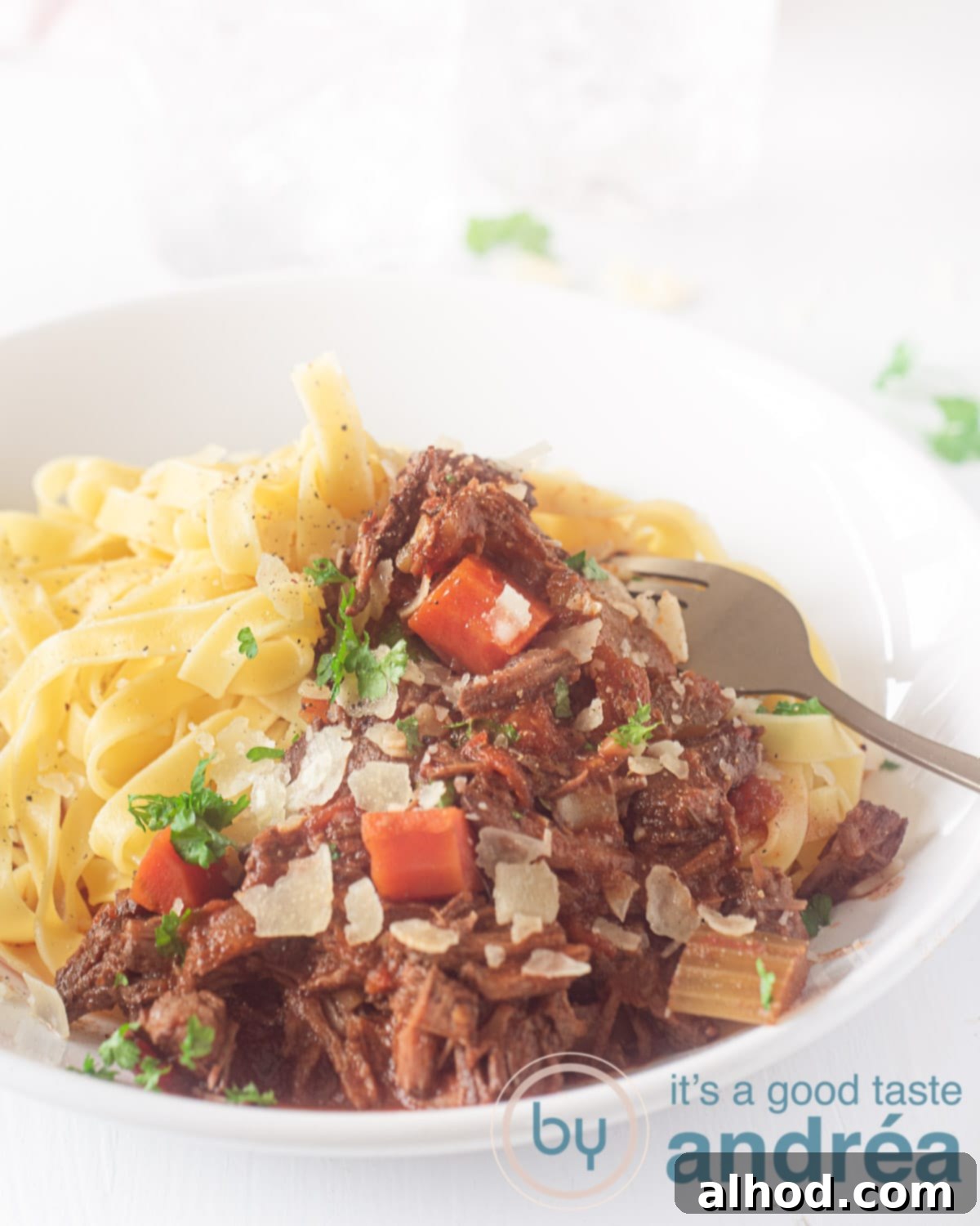 A white plate with Papardelle and Italian stew. A white background. A golden fork pricks the meat