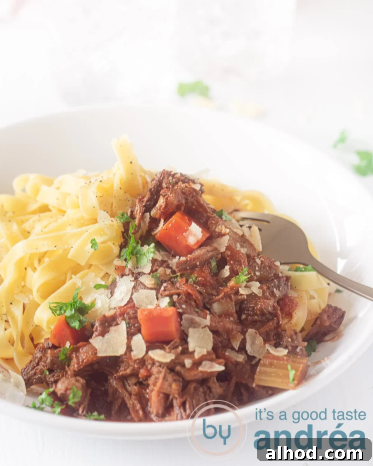 Slow Cooker Beef Ragu with Pasta 2 A white plate with Papardelle and Italian stew. A white background. A golden fork pricks the meat