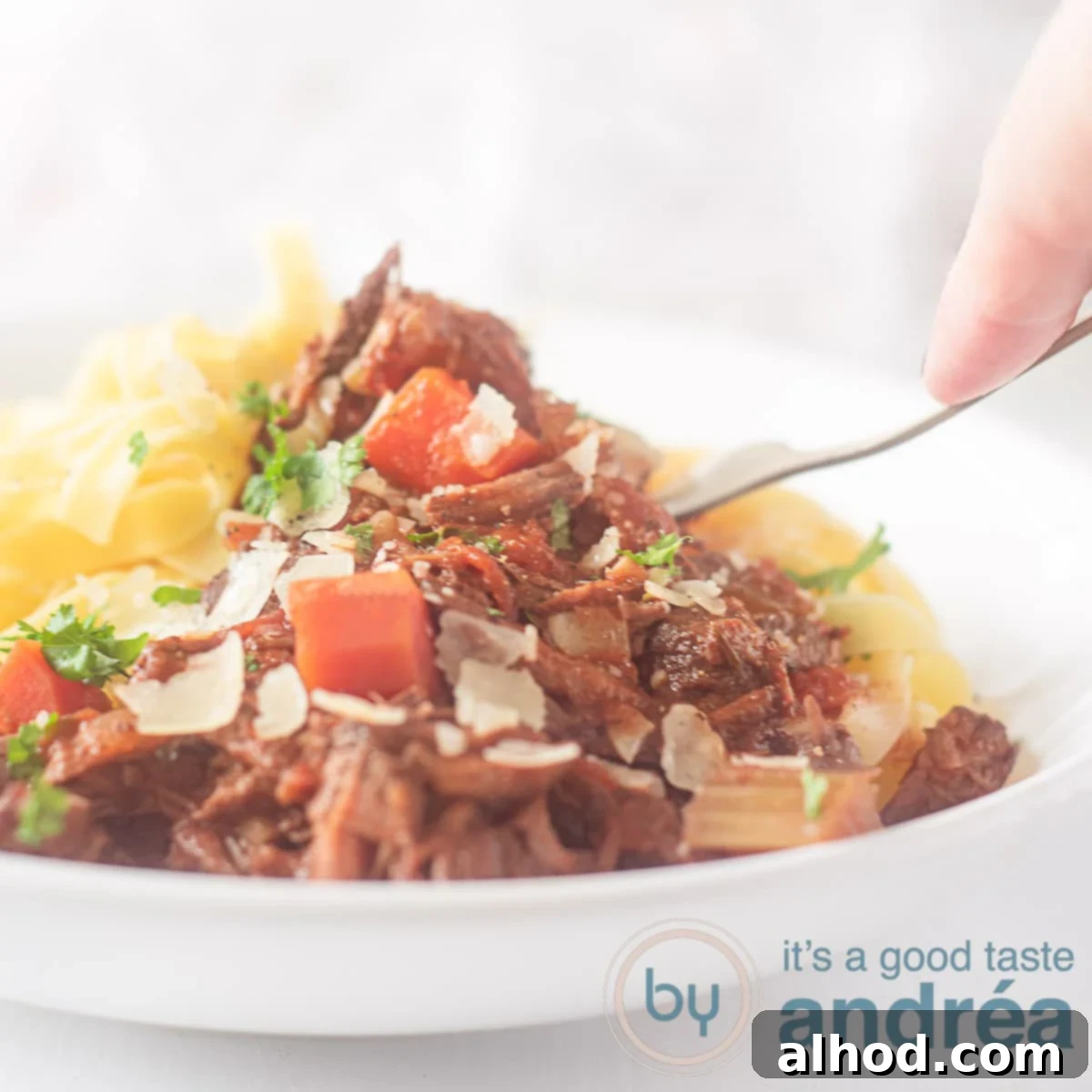 Tender Slow Cooker Beef Ragu with Pasta 6 A square photo with a white plate filled with pappardelle and beef ragout with carrot and Parmesan cheese. A fork pierces it.